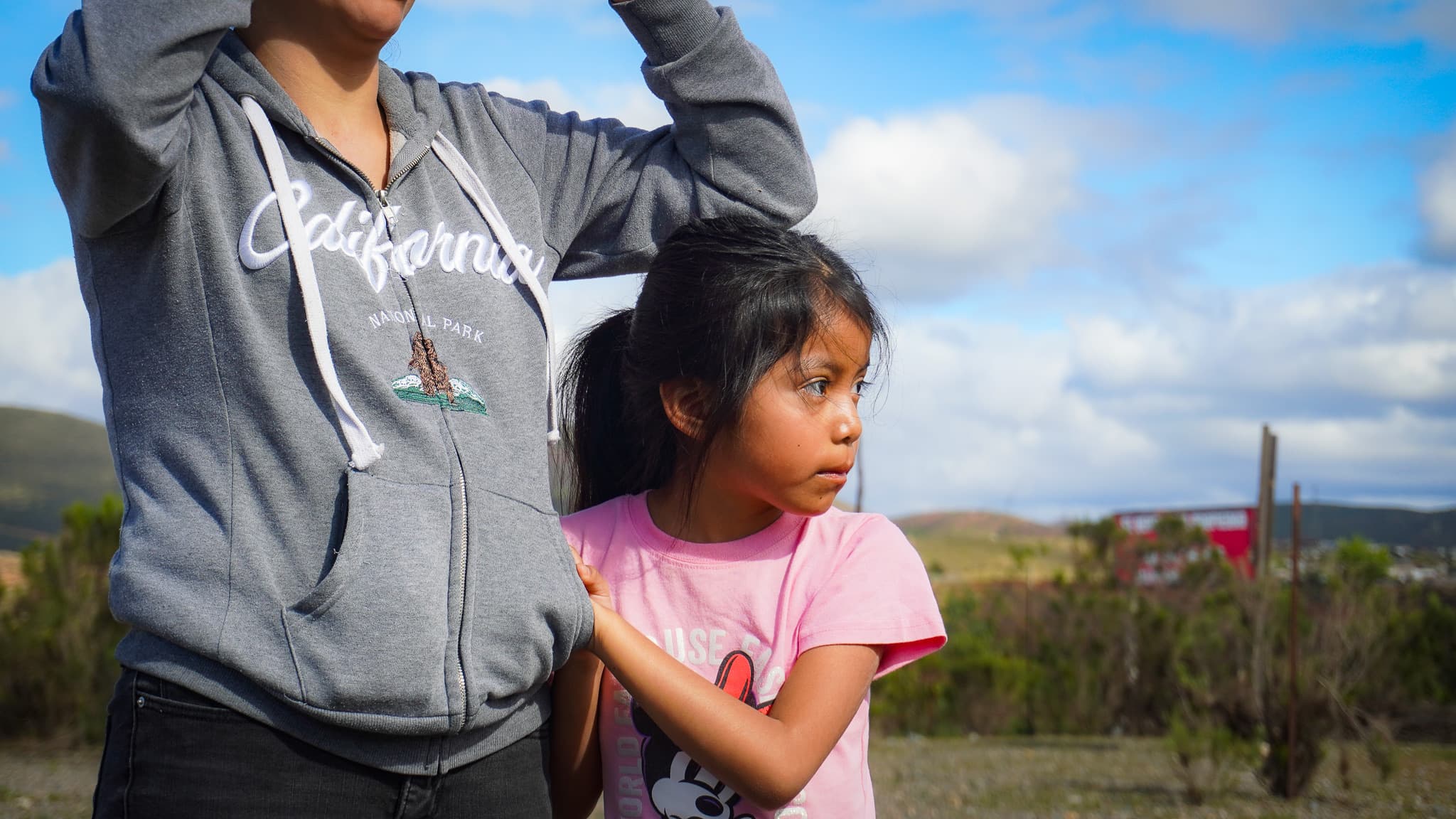 Dulce, age seven, in a pink shirt, holding her mother's arm at the build site