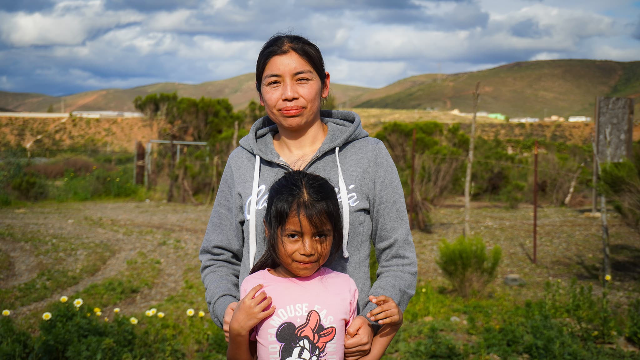 Alma and her daughter Dulce of the Morales Cruz family standing on their land near Ensenada, Mexico, hills behind them