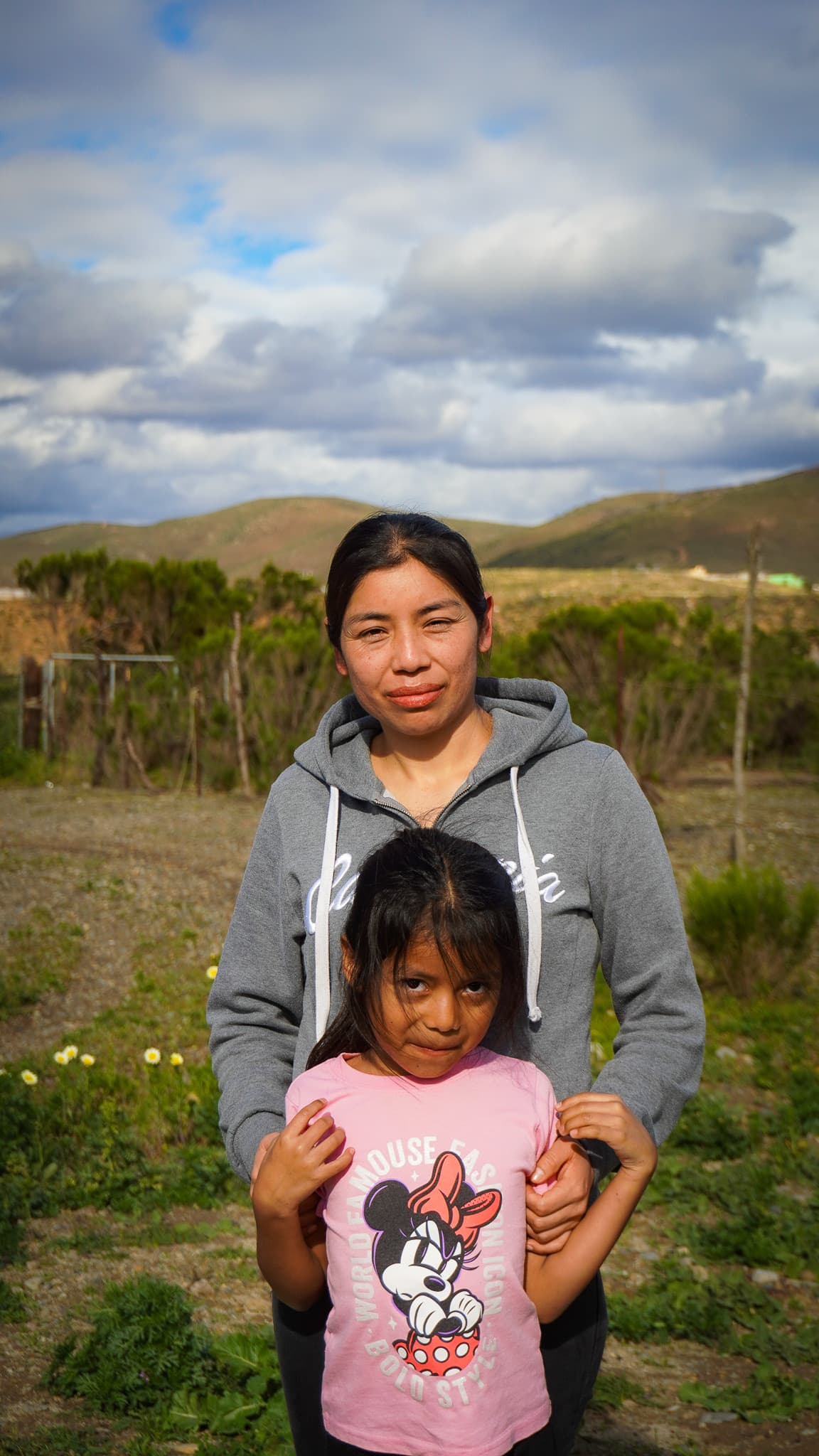 Alma Morales Cruz standing behind her daughter Dulce on the land where their home will be built