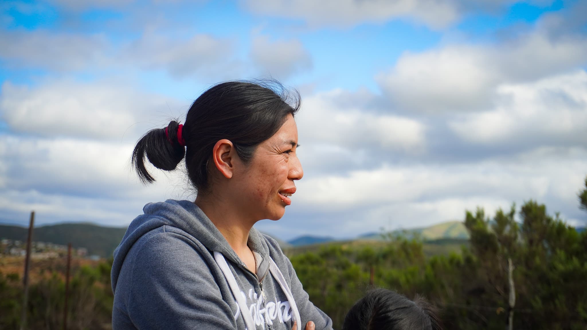 Alma Morales Cruz smiling in profile at the build site, hills and sky behind her