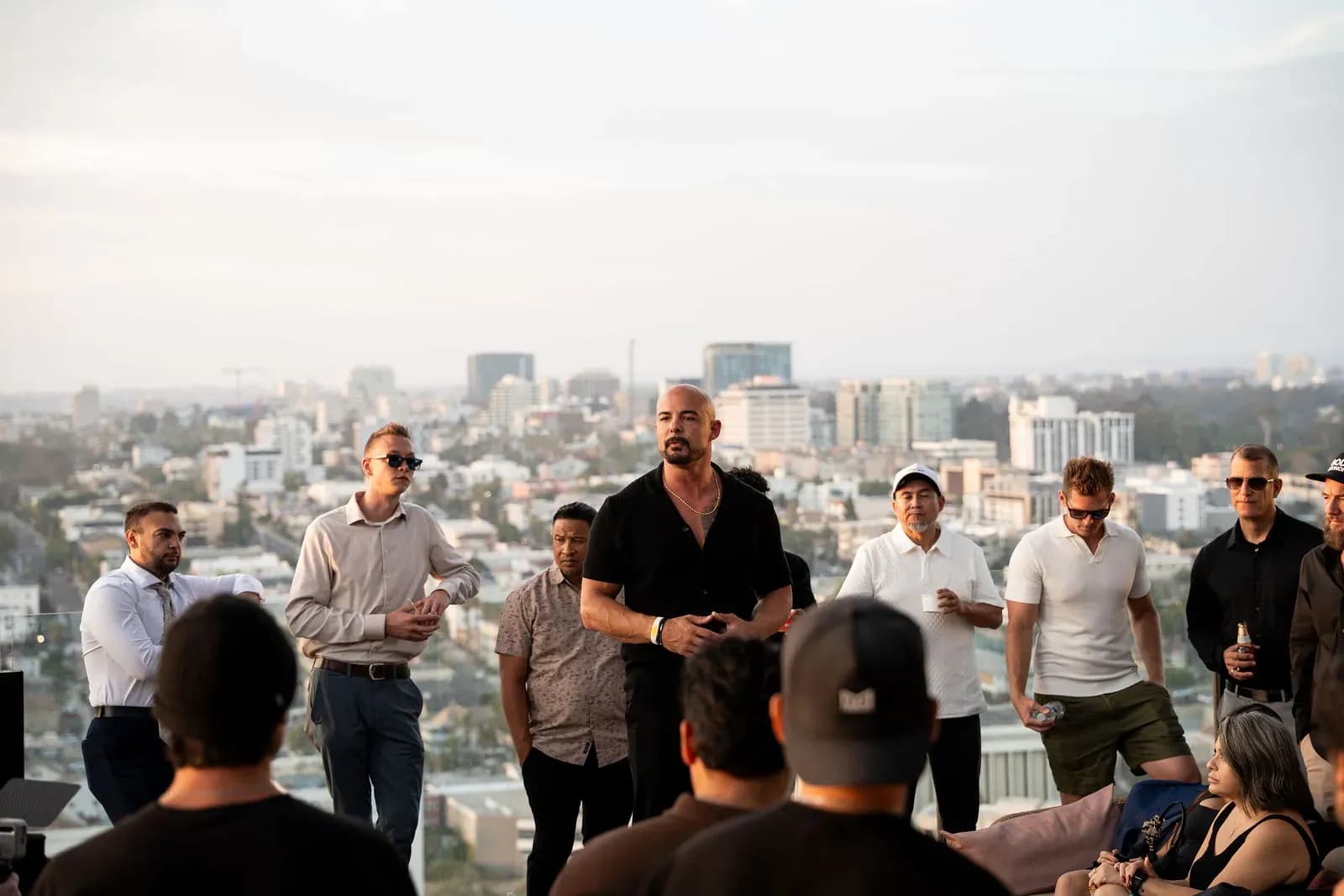 Garin Heslop speaking to a group gathered around him on a rooftop at dusk, the city behind him
