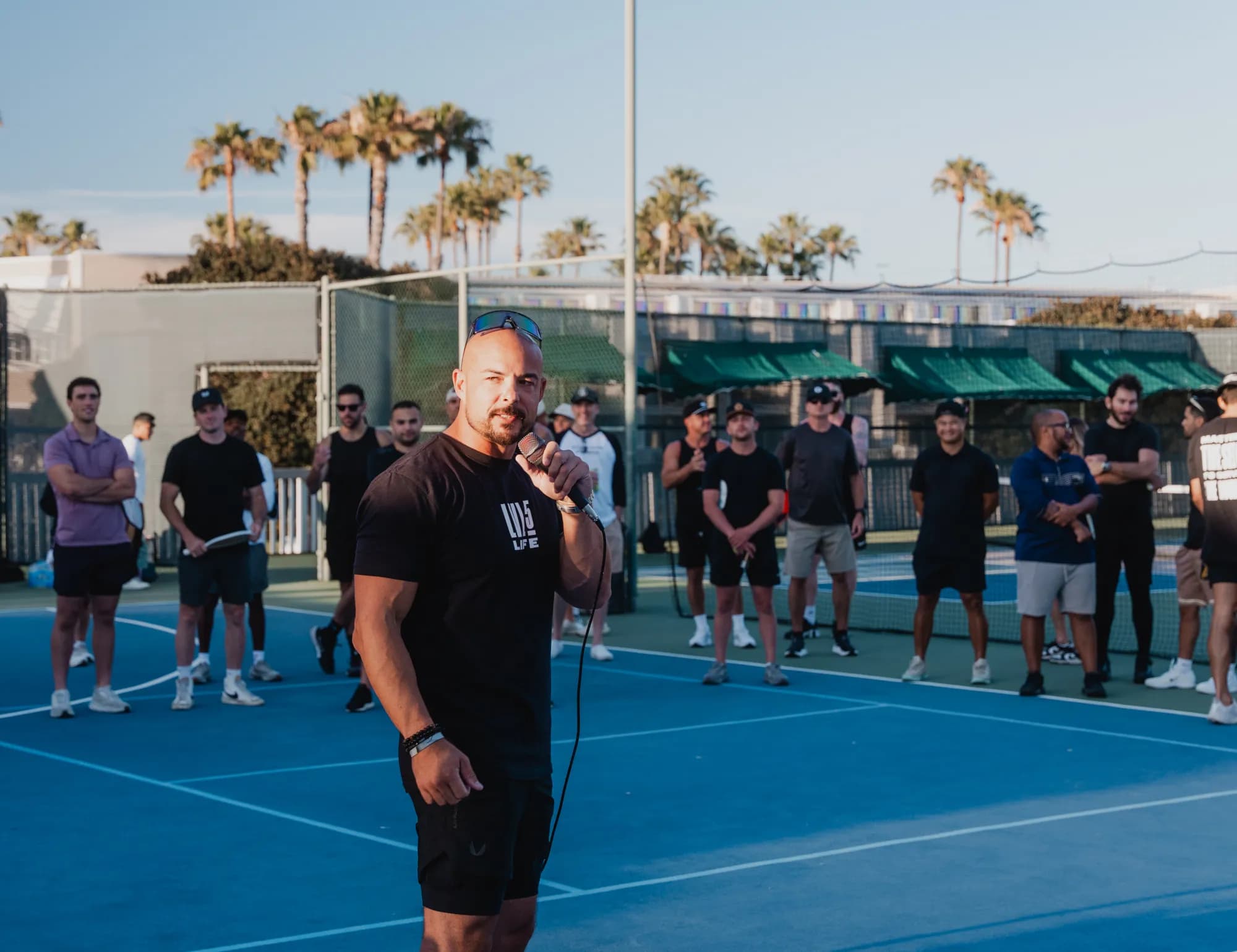 Garin Heslop speaking into a microphone to a group of men on an outdoor court