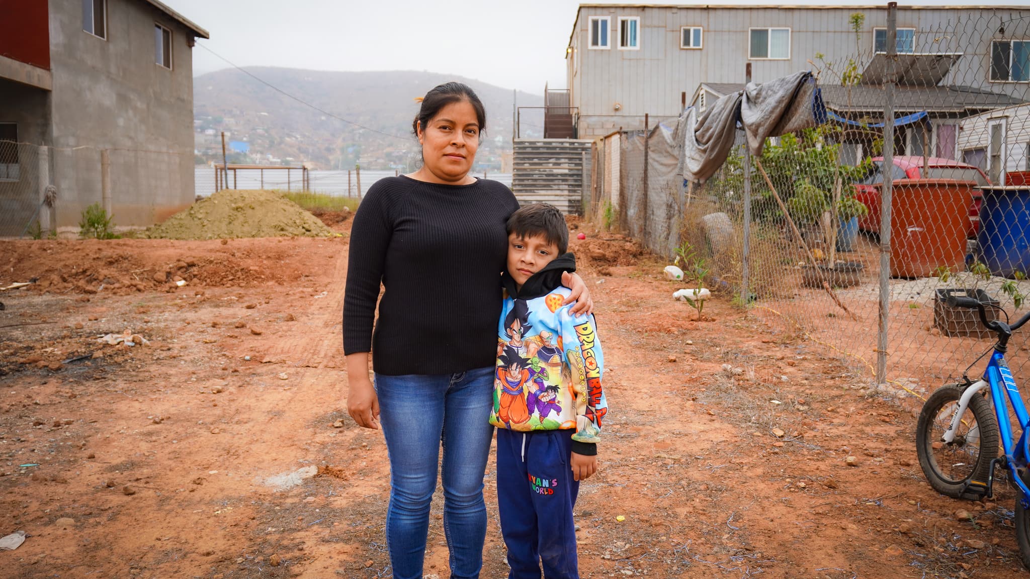 Mother and son of the Pérez Vázquez family standing on the empty dirt lot where their new home will be built in Ensenada, Mexico
